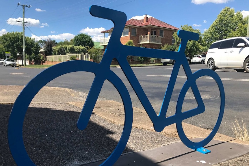 A blue metal bike cut out sign on a footpath with a suburban street behind