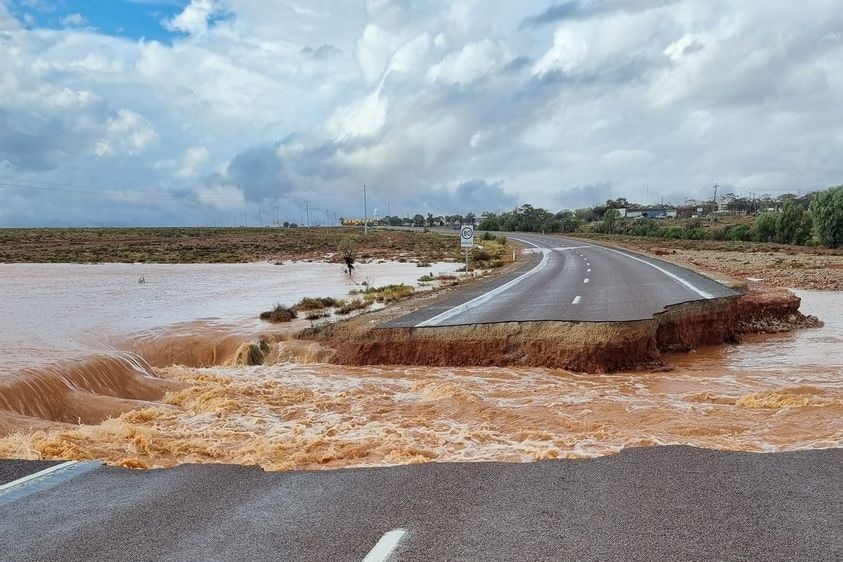 A damaged two-way highway with mud in and water in the middle under a cloudy sky.