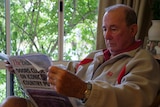 Mr Sisley, older gentleman, reads a copy of The Morning Bulletin next a window in his home.