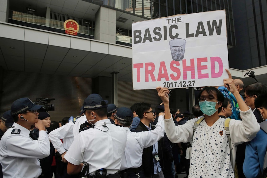 A masked man holding a protest sign stands next to security guards.