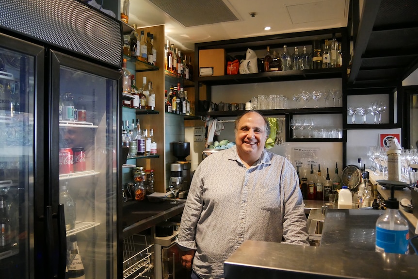 A smiling man stands behind a bar