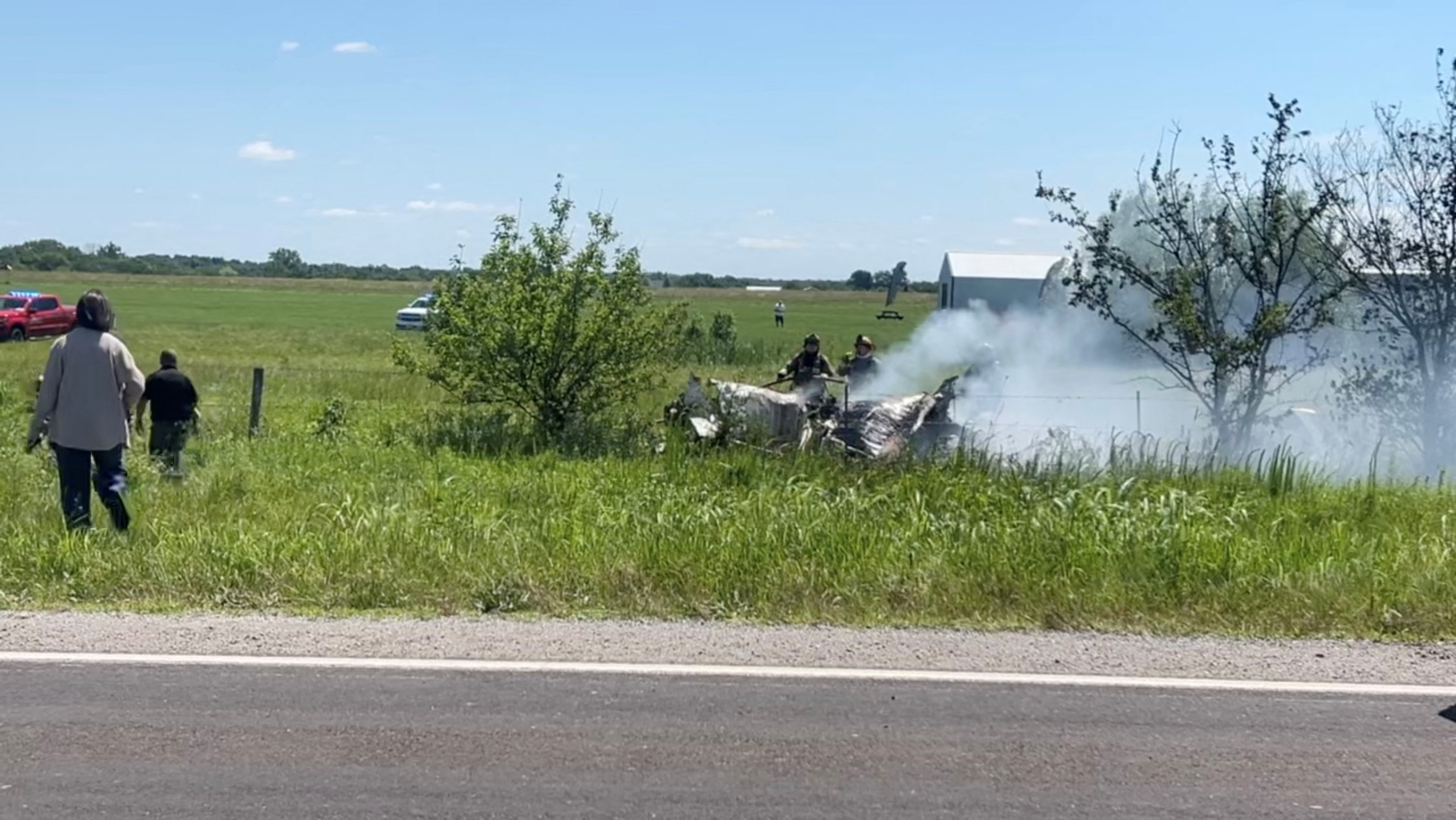 Smoke billows from a crashed plane in a field of grass