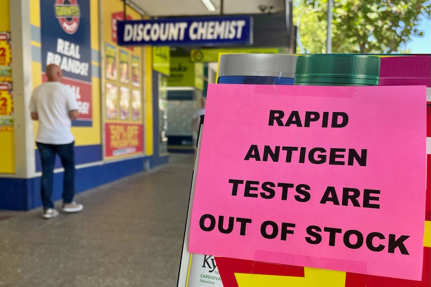 A pink sheet of paper with black text reads 'RAPID ANTIGEN TESTS ARE OUT OF STOCK'.
