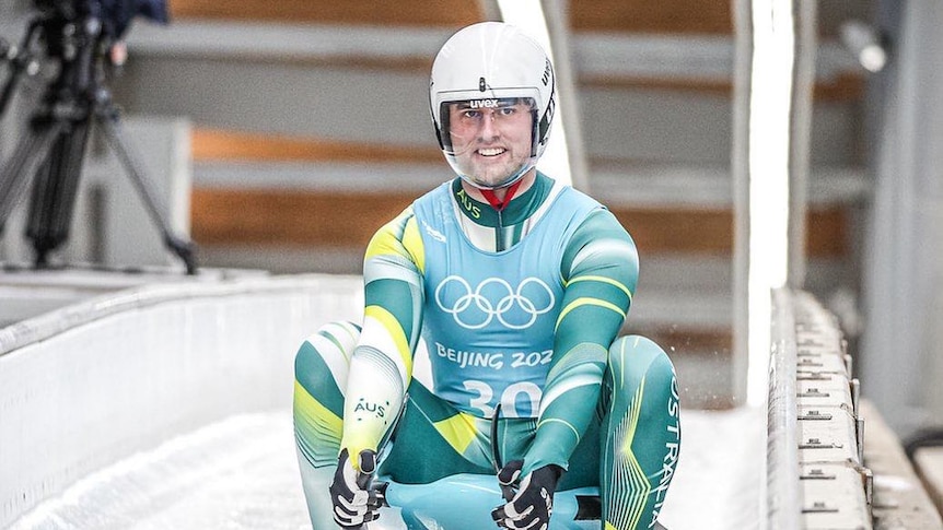 man in olympic uniform sits on luge sled on ice track
