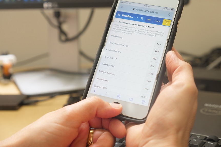 A pair of hands hold a smartphone that has a betting app opened