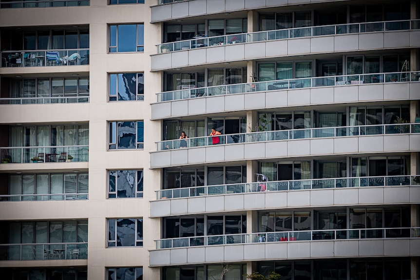 Two people stand on the balcony of an inner city apartment building.