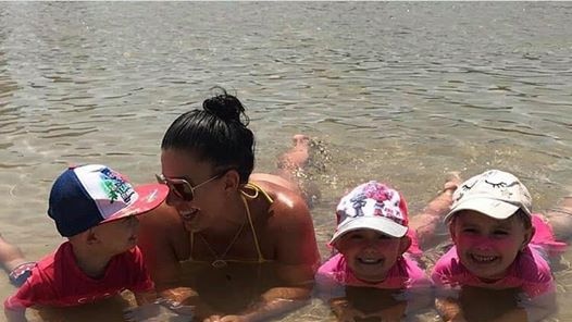 Hannah Baxter with her children at the beach, laying down in the water with her three children.