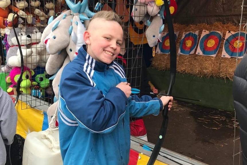 A young man smiles while holding a a bow at a sideshow alley stall.
