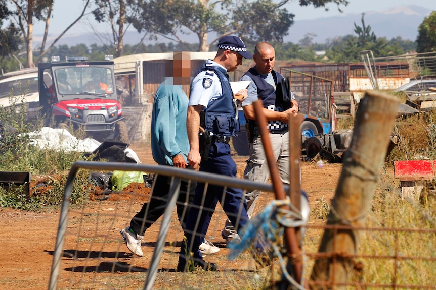 Police accompany a man at a property at Rockbank, west of Melbourne.