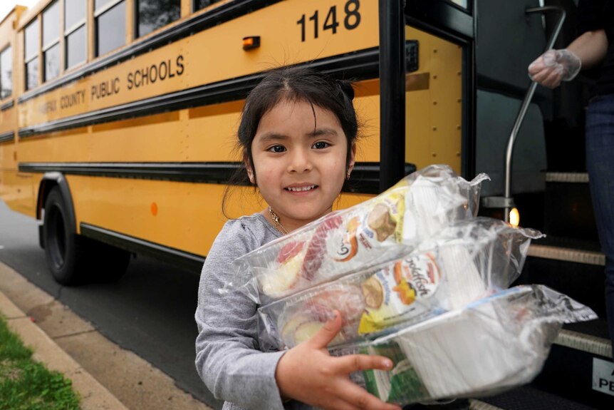 A little girl clutching food next to a school bus