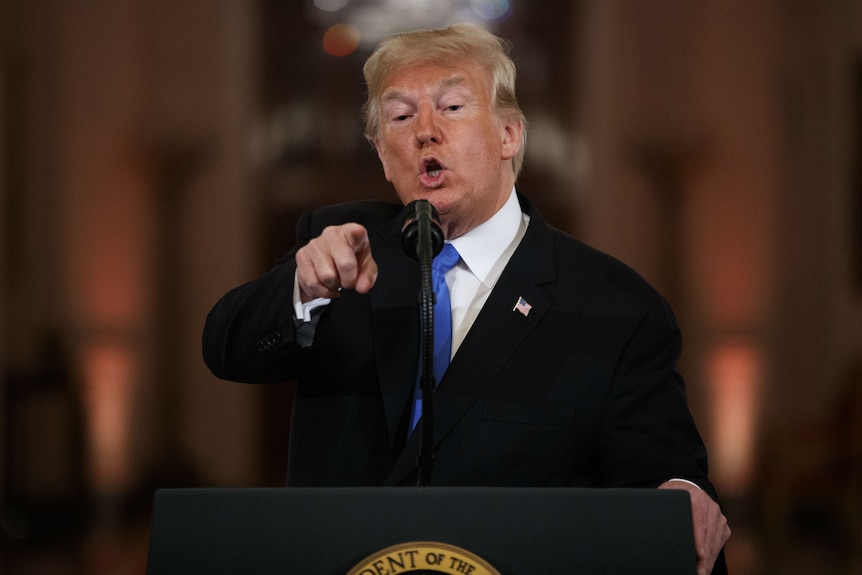 Donald Trump, speaking into a microphone, while pointing a finger at a news conference.