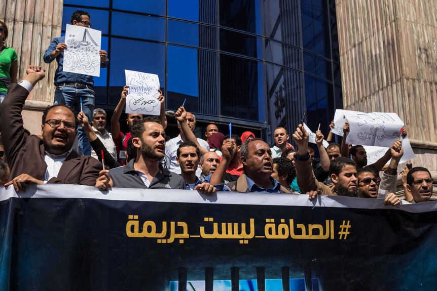 Egyptian journalists hold up pens and a banner
