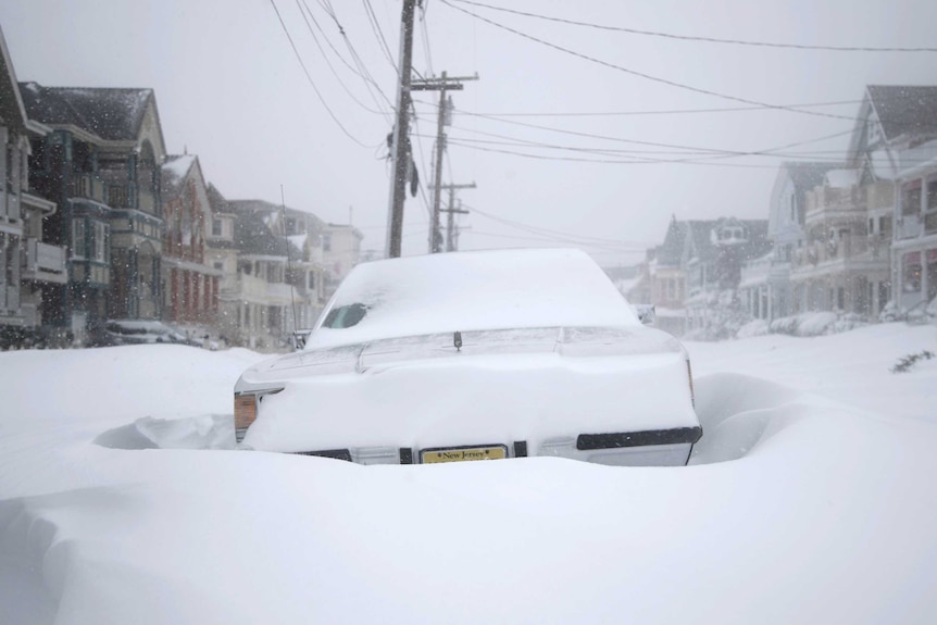 A white car is covered in thick snow on a street in New York.
