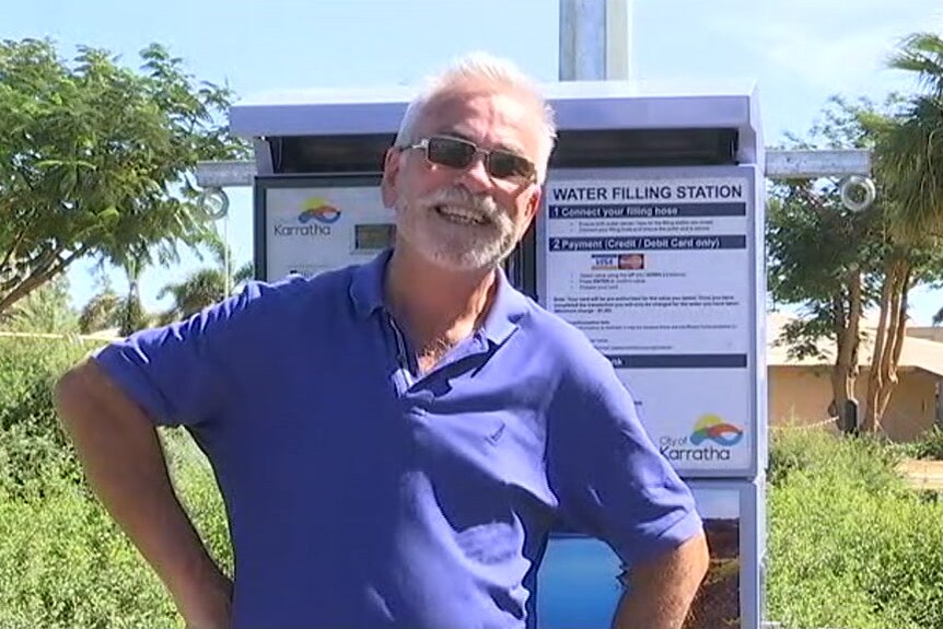 A man in a blue shirt smiling in front of a water-refilling station.