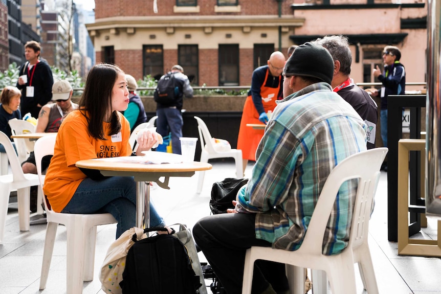 A Sydney Homeless Connect Volunteer talking to two attendees over some lunch.