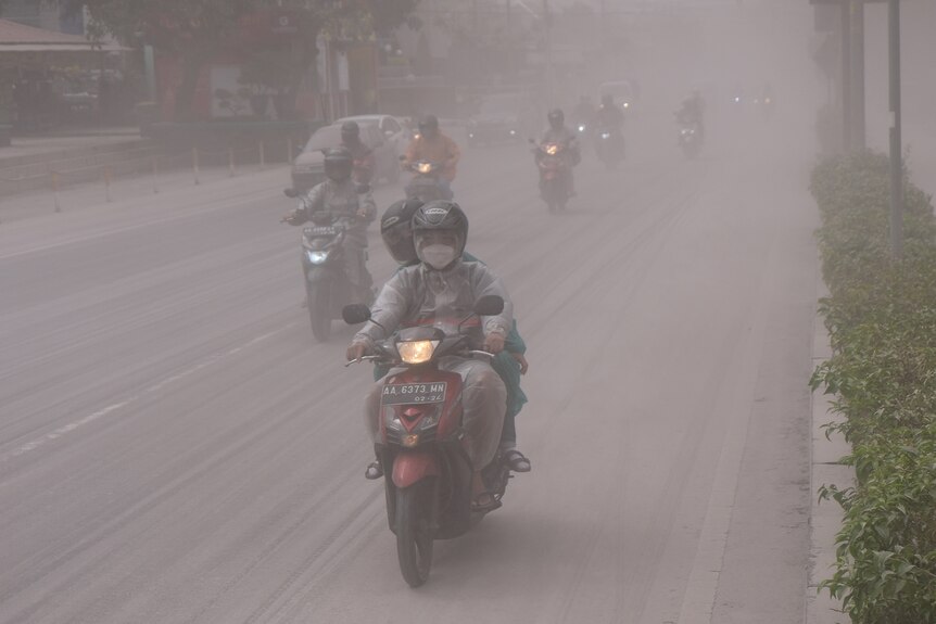 People ride on a road covered by ash from the eruption of Indonesia's Mount Merapi.