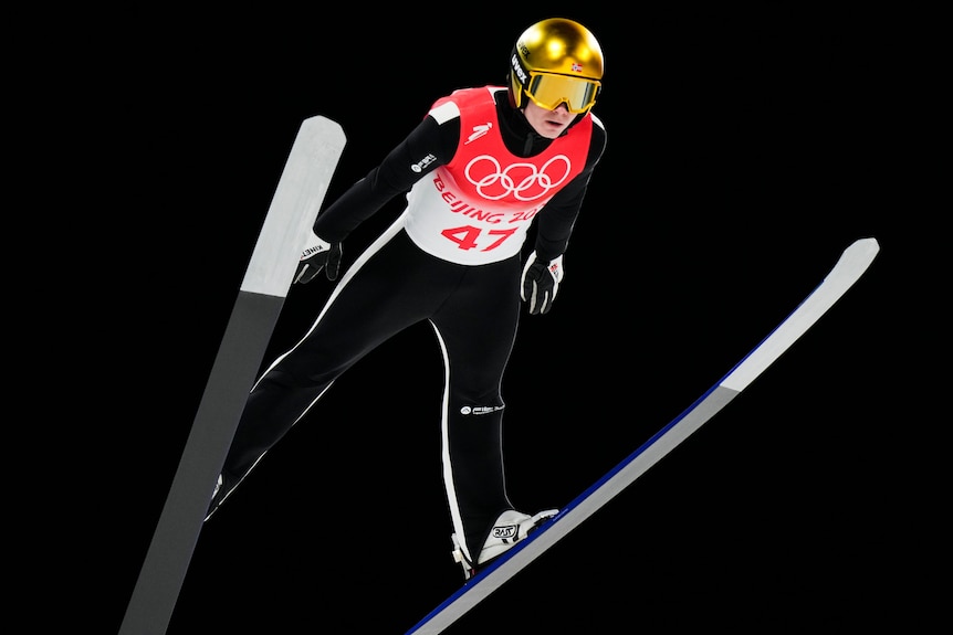 Marius Lindvik soars through the air at night during the ski jumping at the winter olympics
