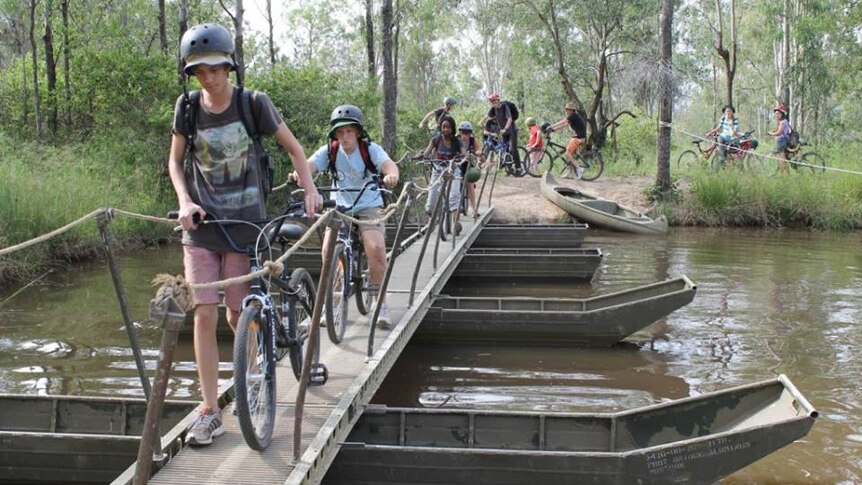 a group of students wheel bicycles along a narrow bridge