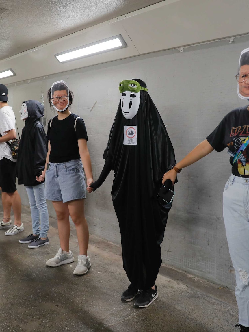 A group of people wearing face masks stand in a walk way, holding hands.