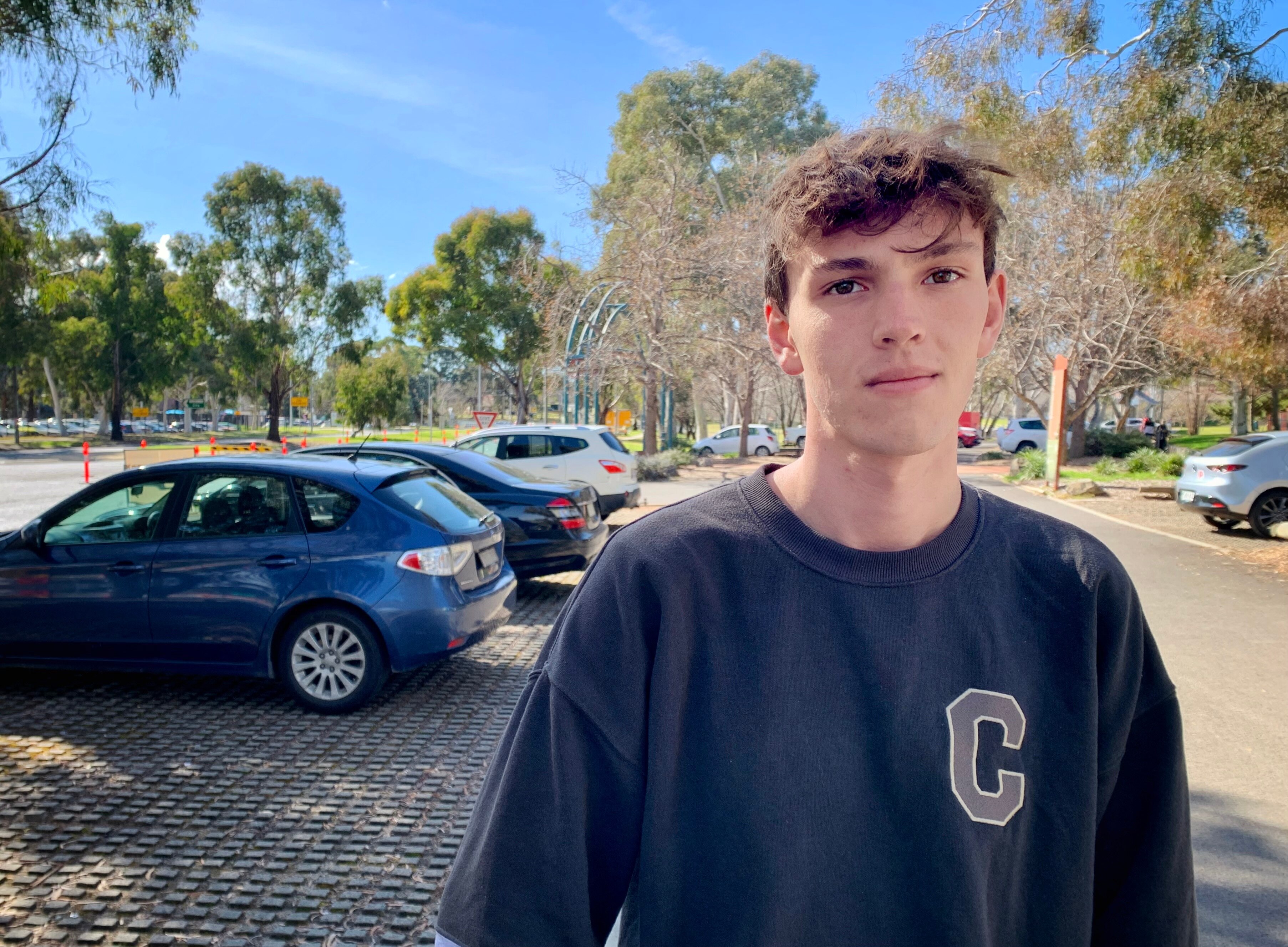 Hugh looks into the camera, standing outside near his car, in the bush.