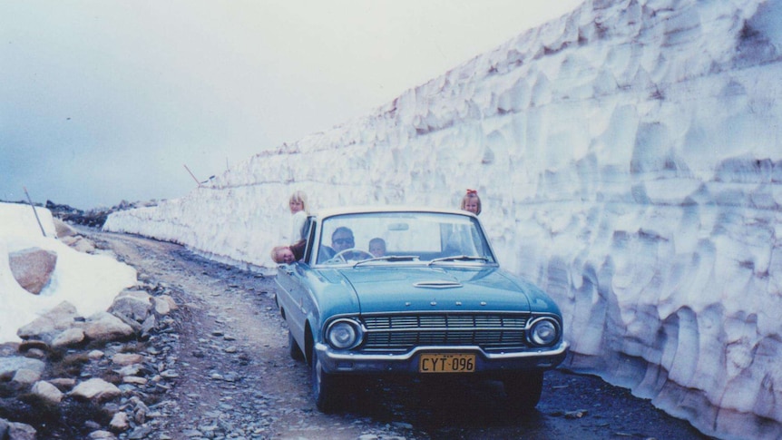 A family drives on a road surrounded by snow.