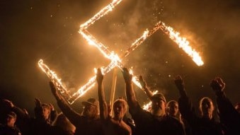 Several people give a Nazi salute in front of a burning swastika.