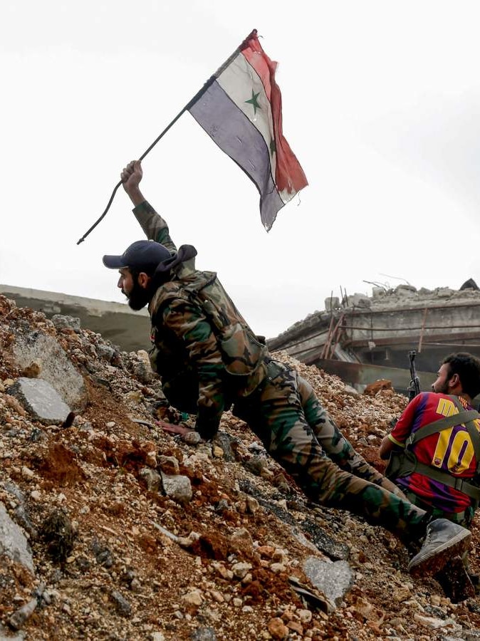 A man plants a Syrian flag in the ground on the frontline.