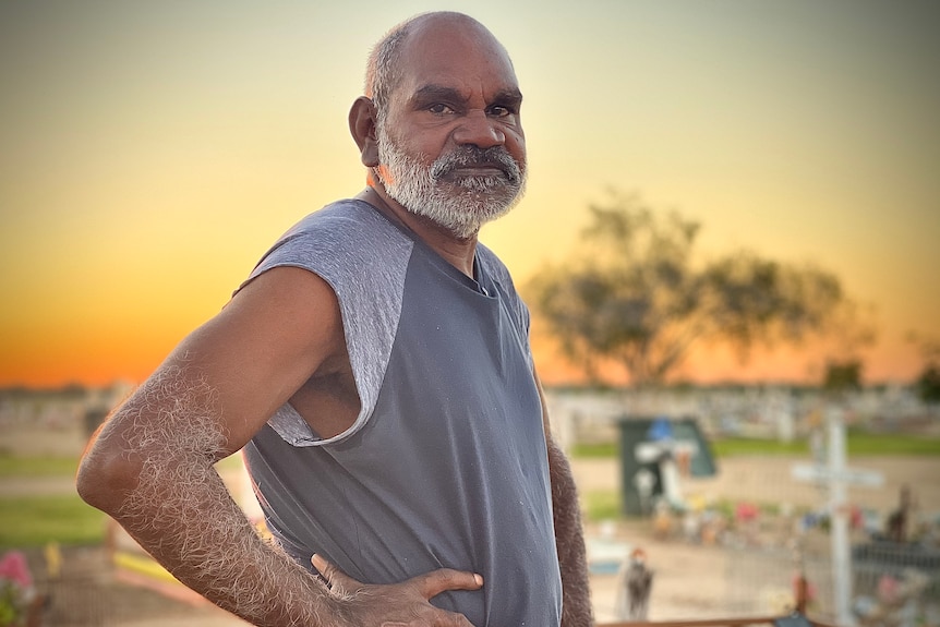 Glen Boney stands in a cemetery with his hand on one hip. The sun is going down in the background.