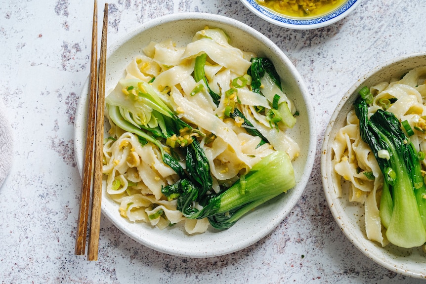 A pair of chopsticks rests on the edge of a bowl filled with noodles and bok choy.