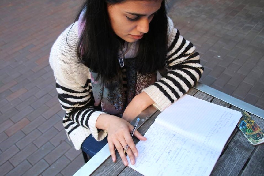 A girl sits at an outdoor table writing in an open journal in front of her.