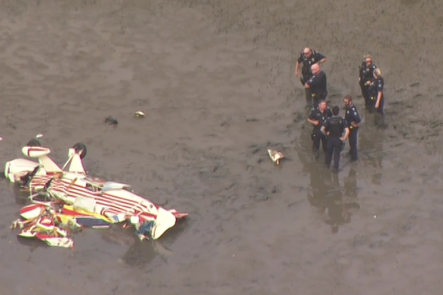 A plane wreck ion a mudflat with a group of emergency workers nearby.