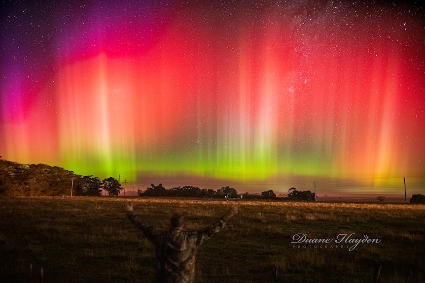 A man with arms out in front of the aurora