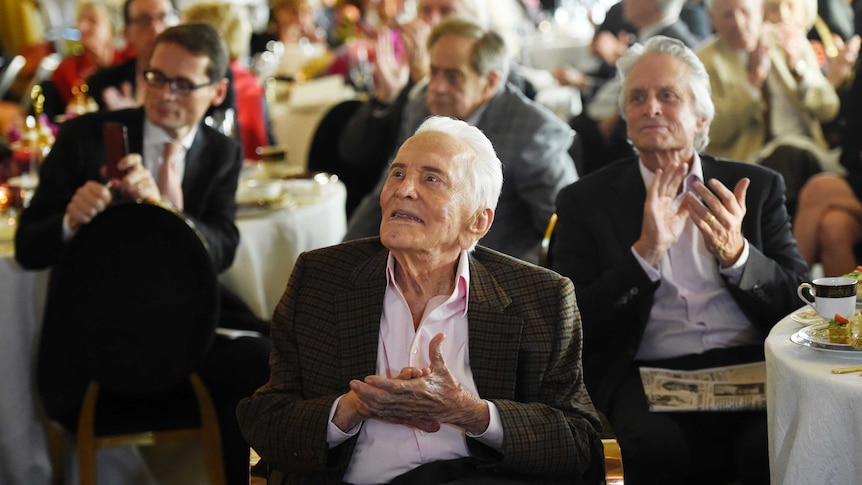Actor Kirk Douglas applauds along with the crowd during his 100th birthday party.