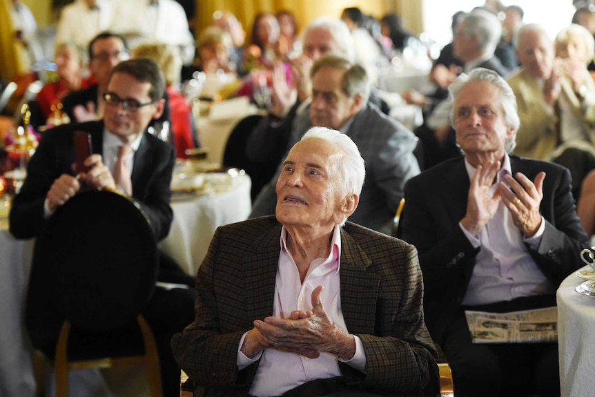 Actor Kirk Douglas applauds along with the crowd during his 100th birthday party.