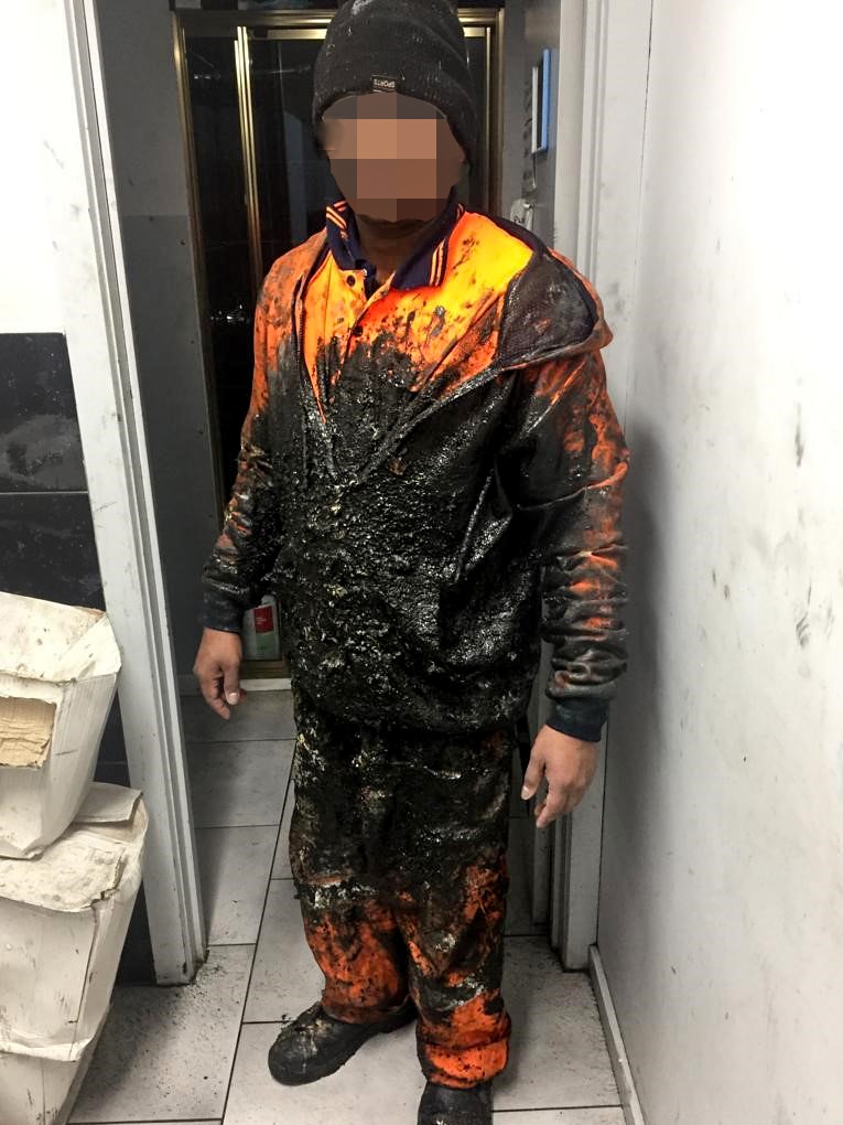 Man in orange cotton uniform covered in black substance with face pixelated.