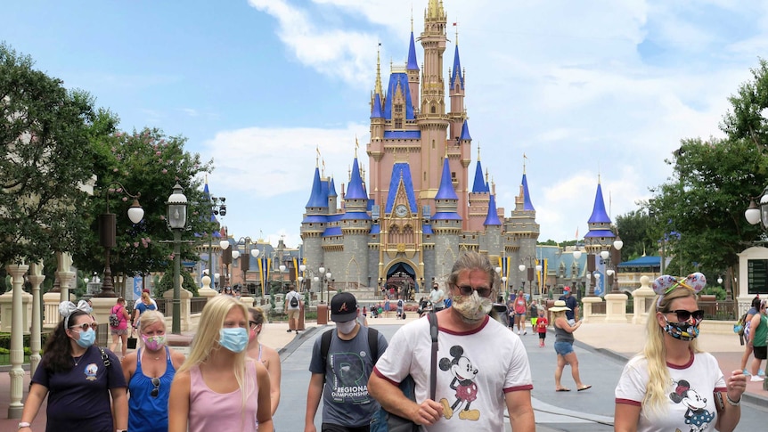 People wearing masks in front of Disney World's Cinderella Castle.