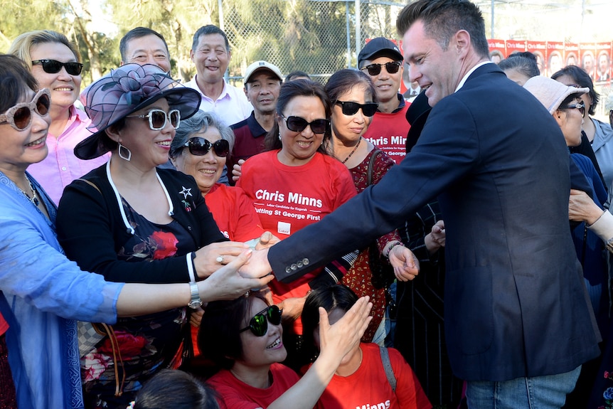 a man surrounded by a group pf admirers all wanting to shake his hand