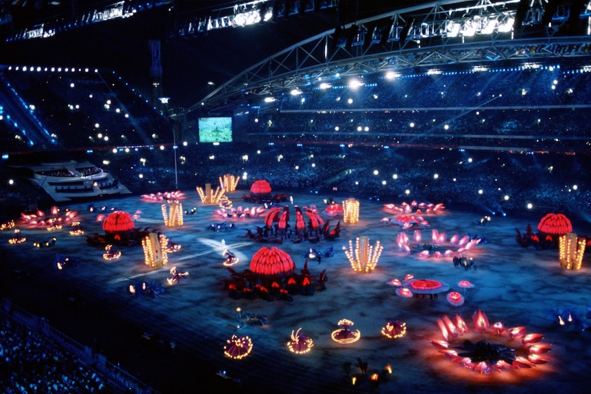 A stadium filled with people watching performers dancing around light sculptures