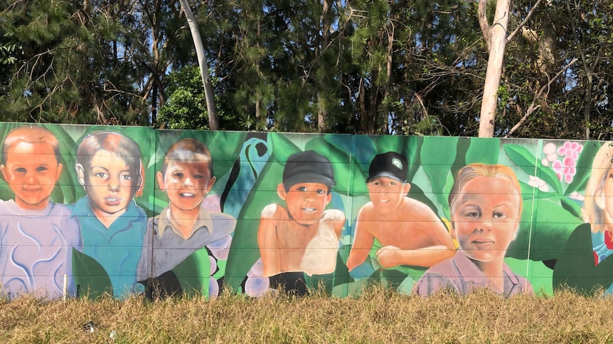 Street art of children's faces painted on a highway soundwall.