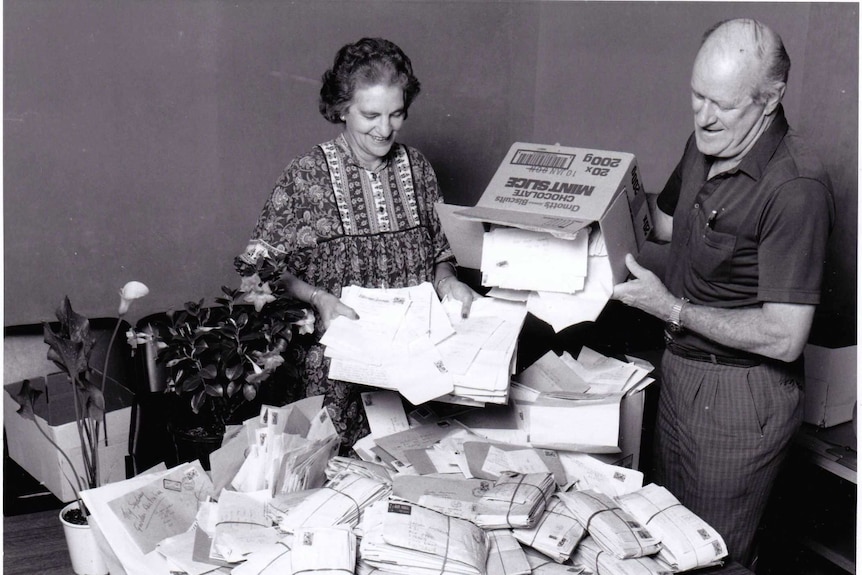 Woman and man tipping out boxes of mail and sorting through letters.