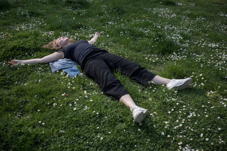 Sofie lies in the grass with her arms out wide. Wild flowers are all around her.