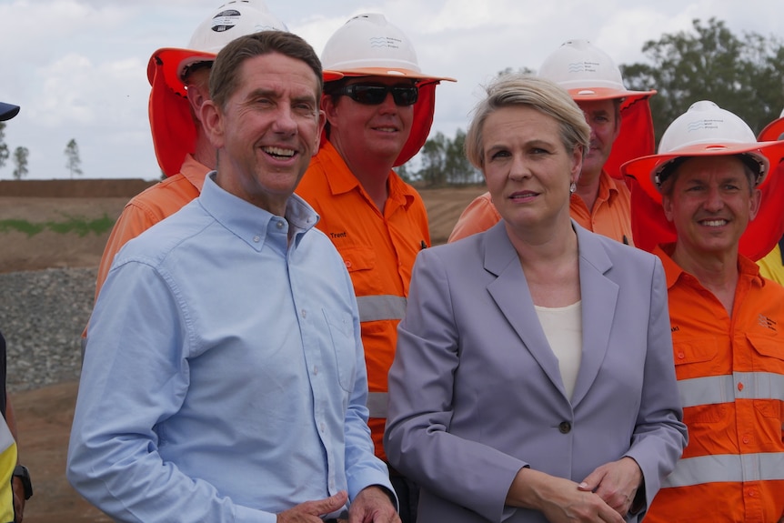 A man and woman in business attire in front of workers in high vis