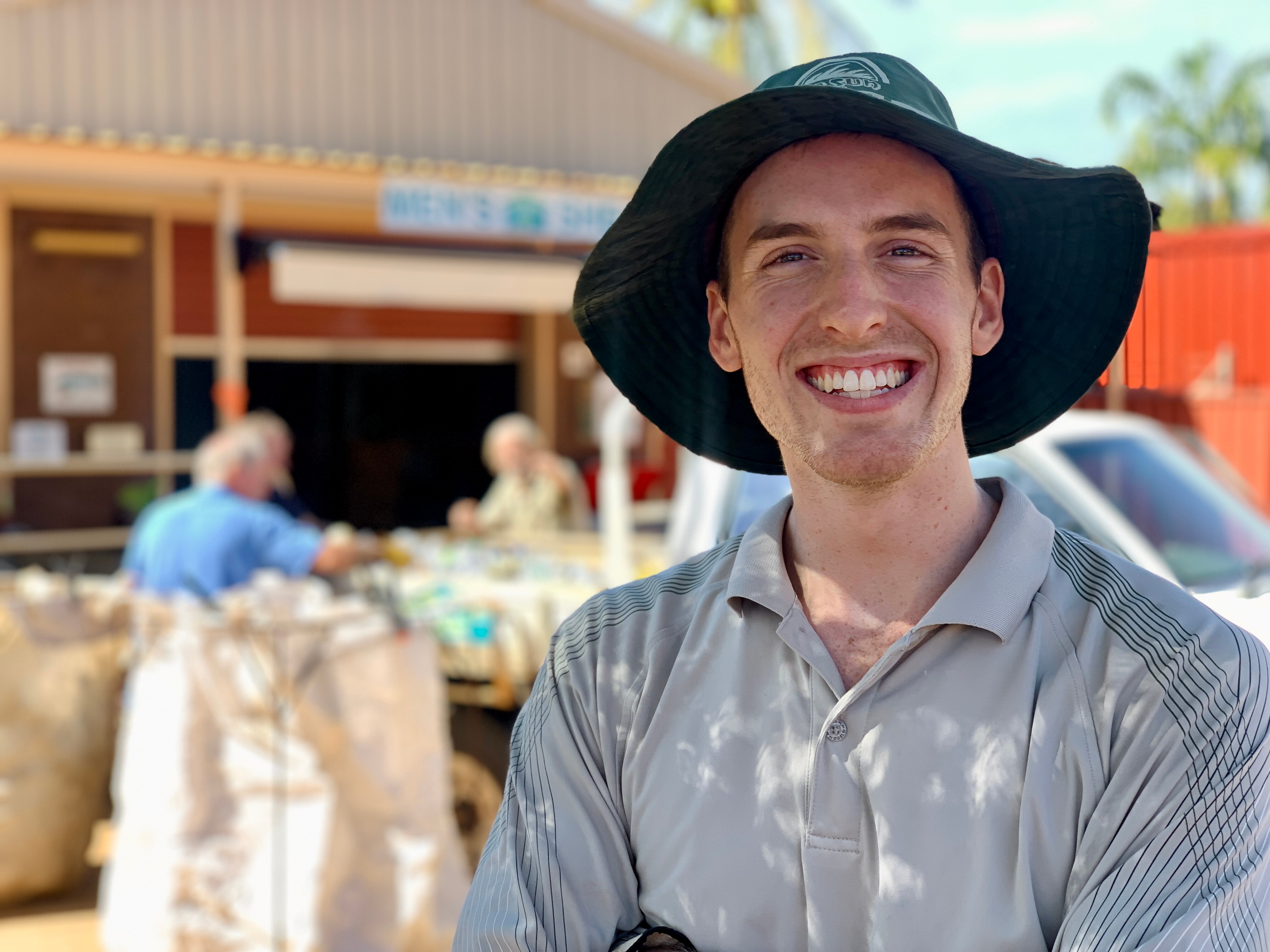 A young man smiles while standing outside in a hat
