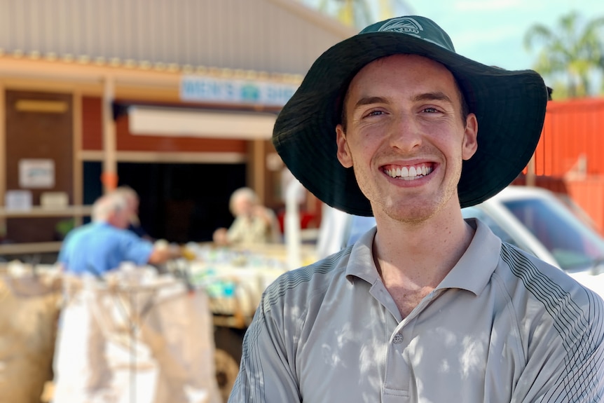 A young man smiles while standing outside in a hat