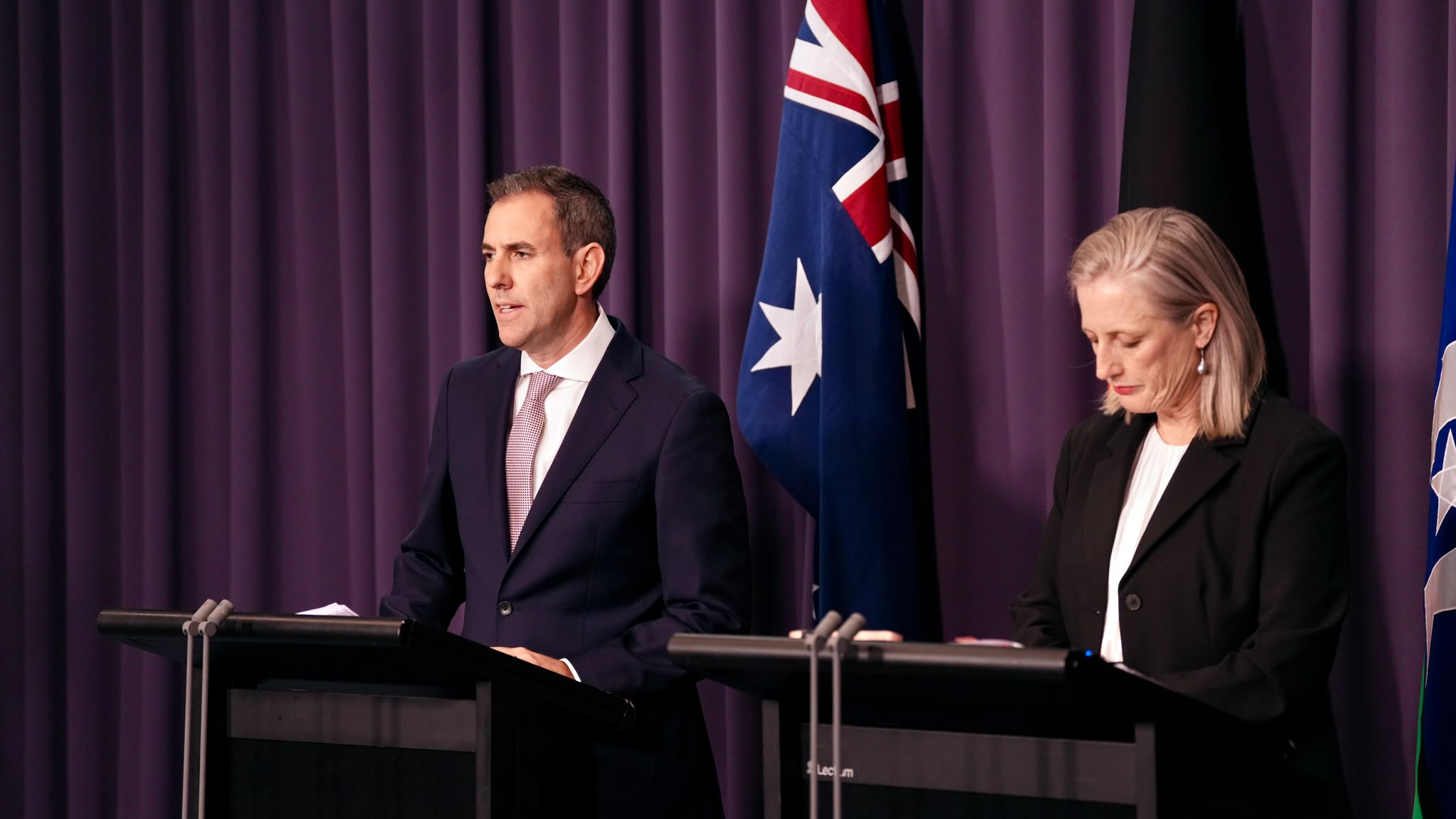 Jim Chalmers and Katy Gallagher speak at a press conference with an Australian flag in the background.
