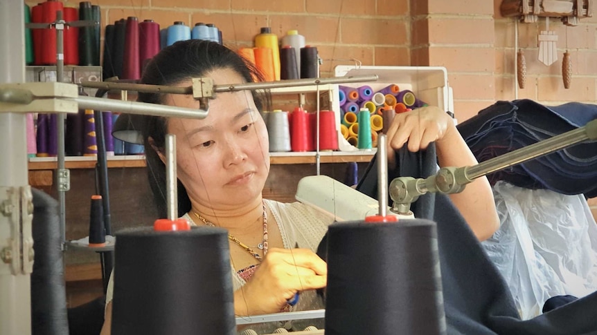 A woman sewing a cloth with a sewing machine from her garage at her home.