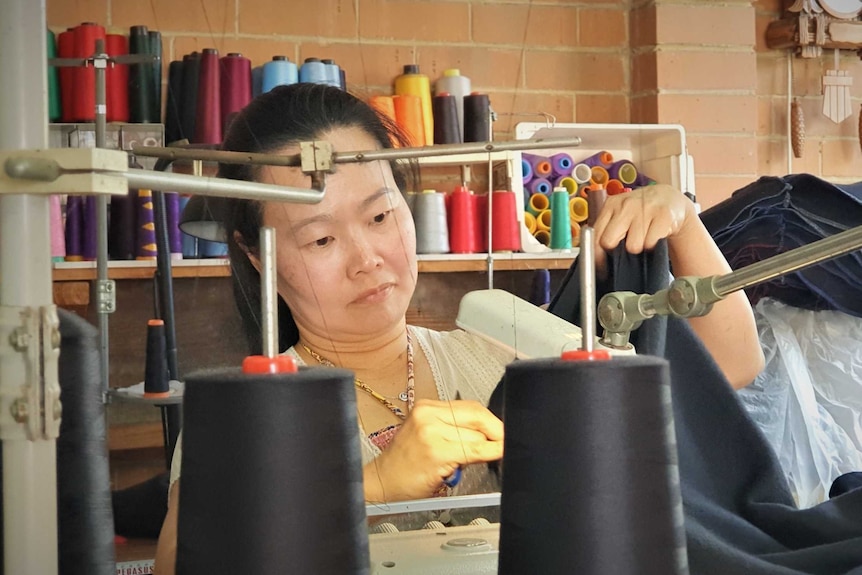 A woman sewing a cloth with a sewing machine from her garage at her home.