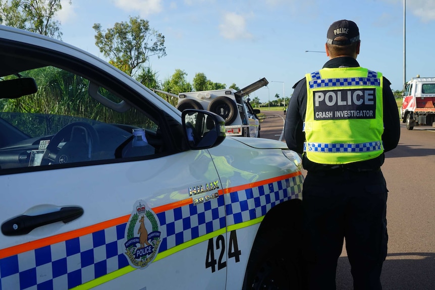 A police officer stands next to a NT Police car.