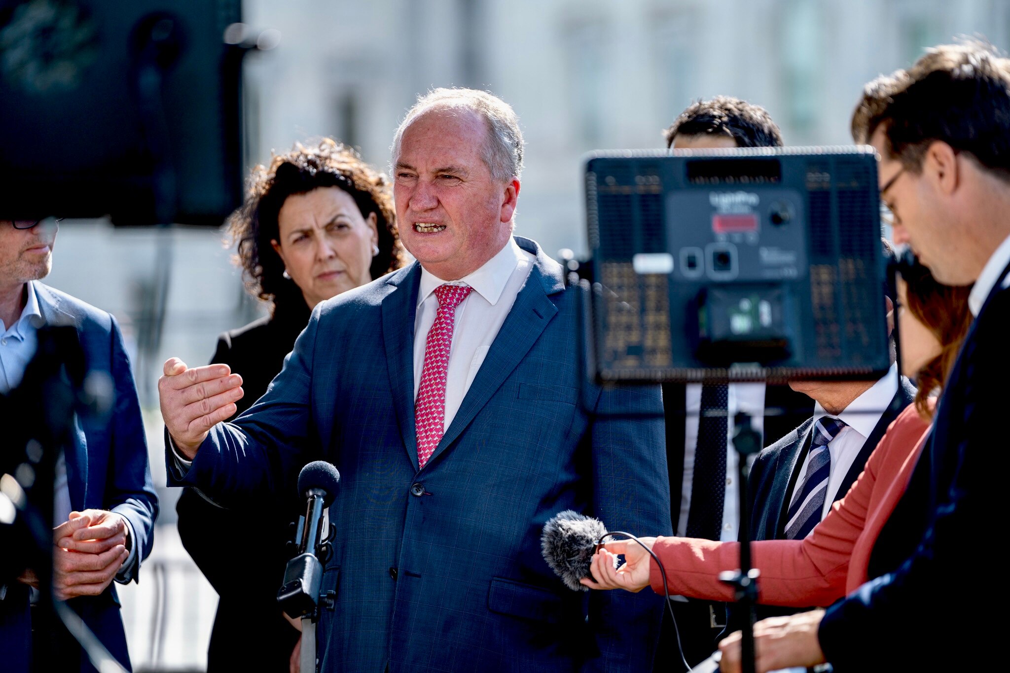 Barnaby Joyce speaks at a press conference, where journalists hold microphones. Other politicians stand behind him.