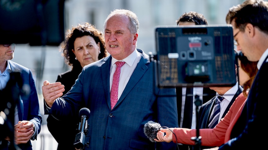Barnaby Joyce speaks at a press conference, where journalists hold microphones. Other politicians stand behind him.